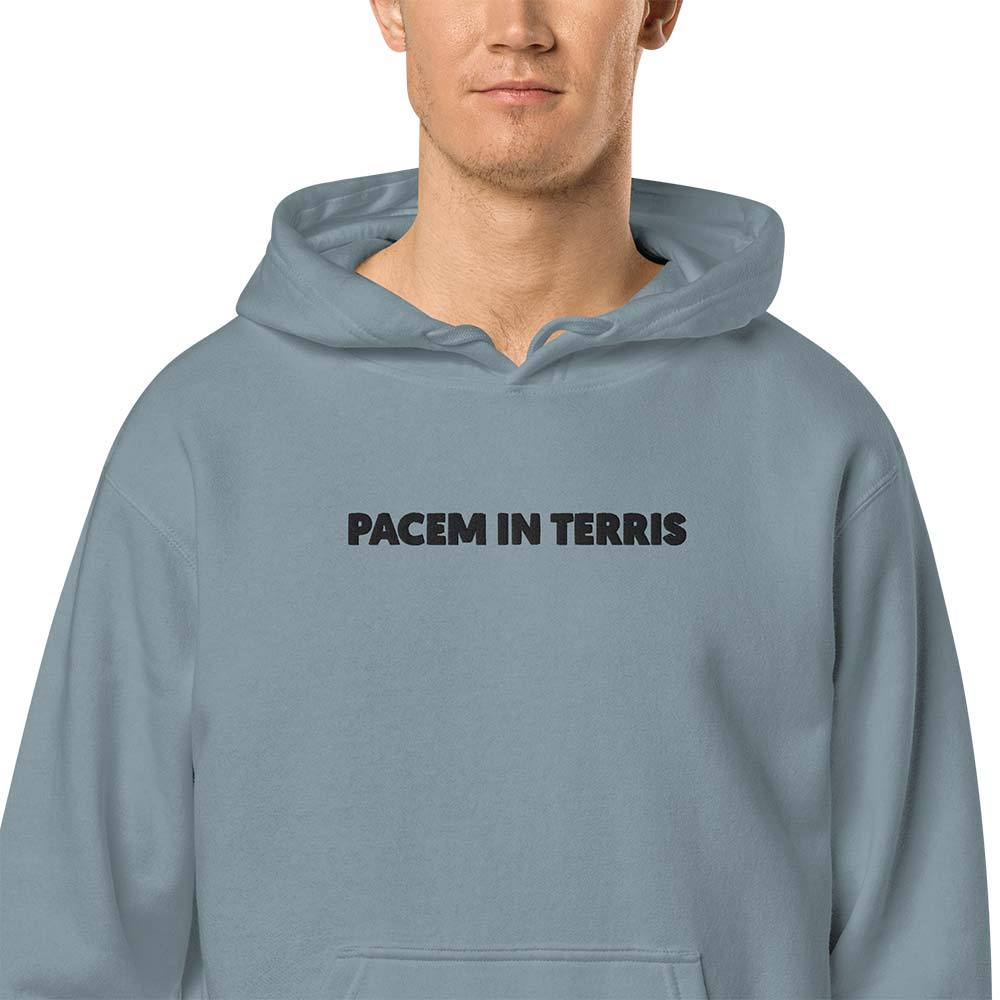 Unisex Vintage Wash Hoodie in Muted Blue. Close-up of a black embroidered motto "Pacem in Terris" on a center chest.